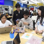 Students smile looking at their device prototype while in the design lab
